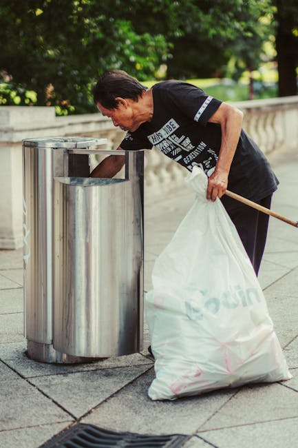 A large pile of black bin bags filled with waste is stacked against a modern, tiled building wall, with some white plastic bottles and other discarded items visible on top or around the bags. The bags are tightly knotted and appear to contain various rubbish, with a few plastic bottles and pieces of paper peeking out from the openings. In the background, part of a cityscape with buildings and a cloudy sky is visible, suggesting an urban environment. The wall behind the waste display features large, beige tiles with visible grout lines, and there is red graffiti text that reads 'XEN' spray-painted on the wall. The scene is lit by natural daylight, casting shadows on the bags, and the overall impression indicates an instance of informal or unscheduled rubbish accumulation, possibly related to private waste handling or on-site clearance carried out by a local waste management service such as Rubbish Collection Kennington, showcasing typical challenges with rubbish removal in public or commercial spaces.